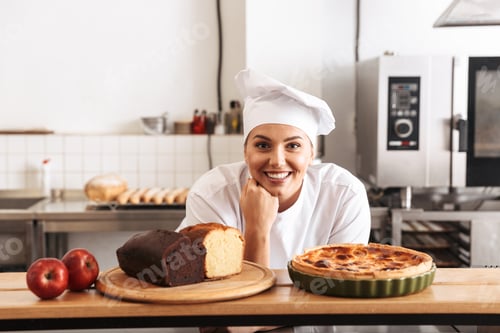 Preview: Image Of Positive Woman Chef Wearing White Uniform Posing In Kitchen At The Cafe With Baked Goods