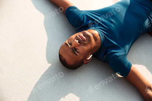 Preview: Close Up Portrait Of A Exhausted Young African Fitness Man In Earphones Resting While Lying On A