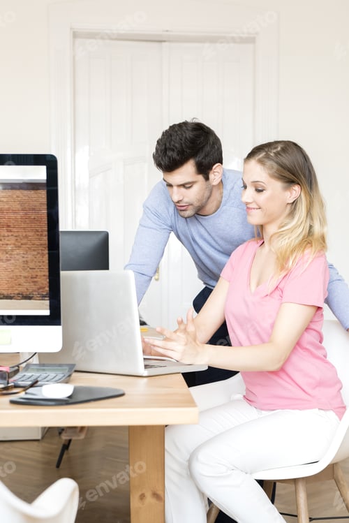 Preview: Shot Of Two Young Business People Sitting In Front Of Laptop And Consulting While Working On New