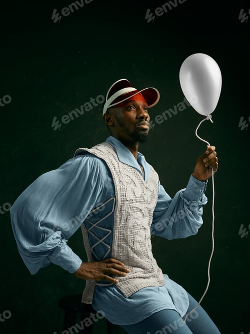 Preview: Young Man As A Medieval Grandee Or Nobleman On Dark Studio Background. Sitting In A Cap With The