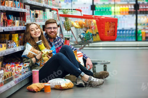 Preview: Young Woman With Big Amount Of Packs And Her Man Sitting On The Floor Of The Mall Eating Chips