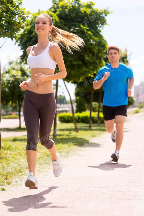 Preview: I Am Winning! Cheerful Young Woman Jogging Along The Road With Man In The Background