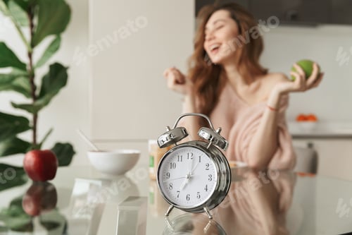 Preview: Close Up Of A Smiling Young Woman Having Healthy Breakfast While Sitting At The Table With Alarm