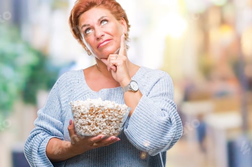 Preview: Atrractive Senior Caucasian Redhead Woman Eating Popcorn Over Isolated Background Serious Face