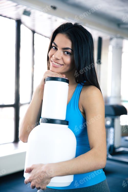 Preview: Smiling Woman At Gym With Sports Nutrition Standing At Gym And Looking At Camera