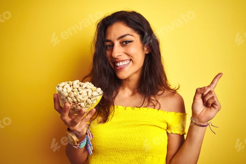 Preview: Young Beautiful Woman Holding Bowl With Pistachios Over Isolated Yellow Background Very Happy