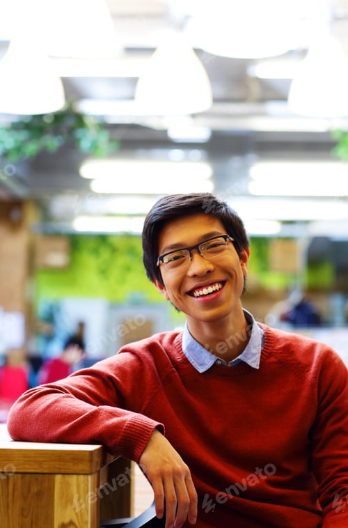 Preview: Young Cheerful Asian Student Sitting At The Table