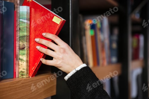 Preview: Close Up Of A Young Women Hand In A Library Taking A Book From The Shelf