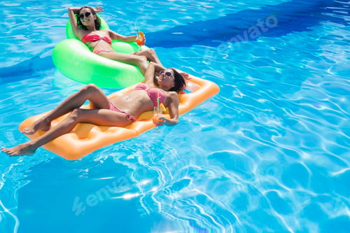 Preview: Two Happy Girls Holding Cocktails And Lying On Air Mattress In Swimming Pool