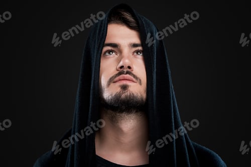 Preview: Mysterious Man. Handsome Young Man In Black Hood Looking Up While Standing Against Black Background