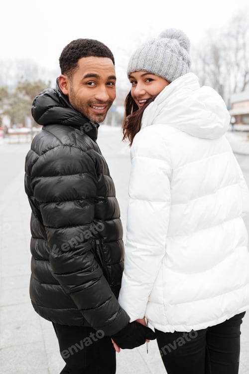 Preview: Cheerful Young Couple Holding Hands And Looking Back Outdoors In Winter