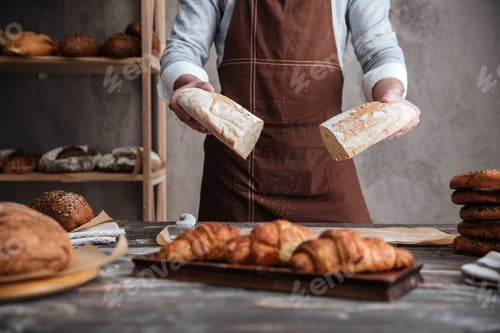Preview: Cropped Photo Of Young Man Baker Standing At Bakery Holding Bread.