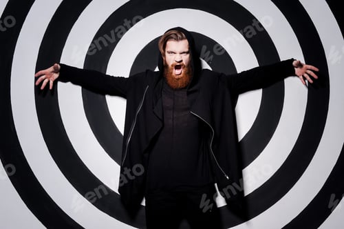 Preview: Mysterious Look. Handsome Young Bearded Man Screaming And Keeping Arms Outstretched While Standing