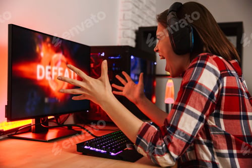 Preview: Angry Girl Gamer Sitting At The Table, Playing Online Games On A Computer Indoors