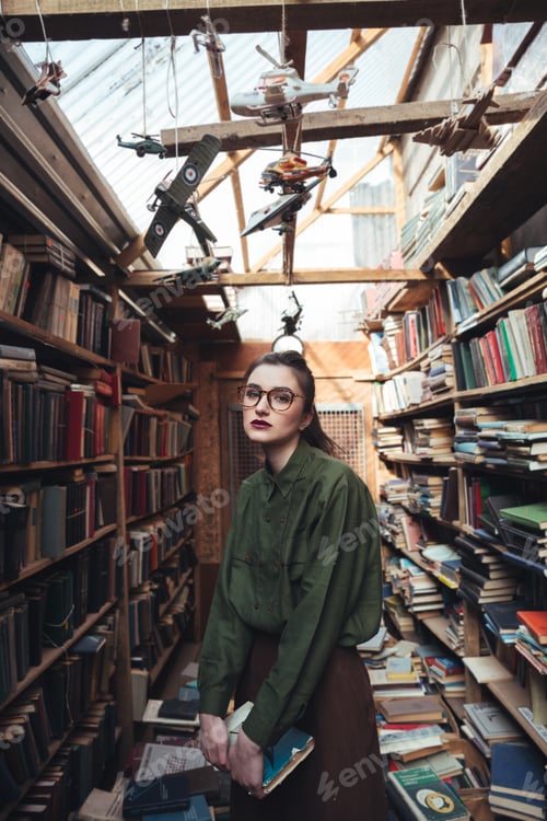 Preview: Portrait Of Young Woman In Glasses Holding Book In Library. Looking Camera