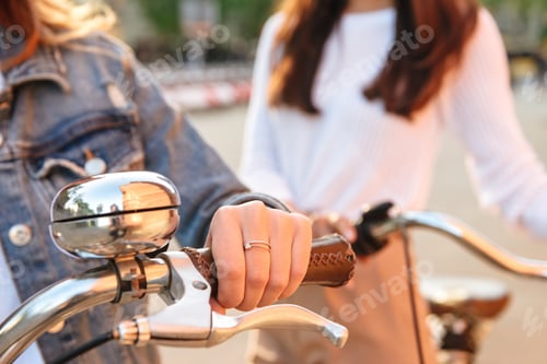 Preview: Cropped Image Of Two Young Women Friends Outdoors On Bicycles In Park.