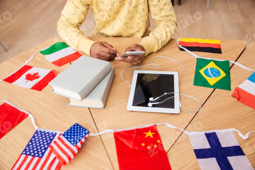 Preview: Closeup Of Man Sitting At The Table With Tablet, Books And Flags Of Countries