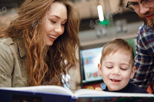 Preview: Cropped Image Of A Young Family Reading Book In Supermarket While Their Son Sitting In Shopping