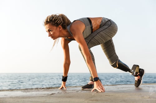 Preview: Side View Of Disabled Athlete Woman With Prosthetic Leg Starting To Run Outdoor At The Beach