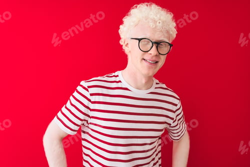 Preview: Young Albino Blond Man Wearing Striped T-Shirt And Glasses Over Isolated Red Background Winking