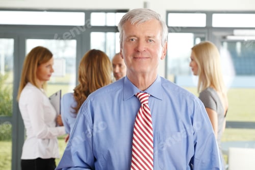 Preview: Portrait Of Senior Businessman Standing At Office While Businesswomen Consulting At Background