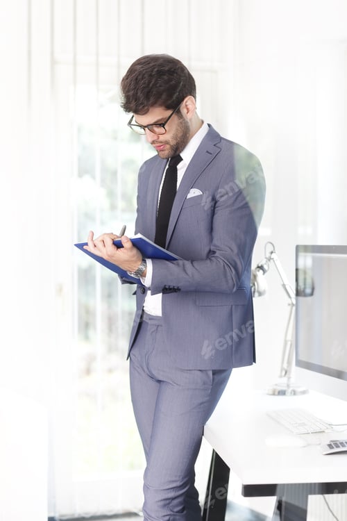 Preview: Portrait Of Young Assistant Businessman Doing Some Paperwork While Standing At His Workplace At