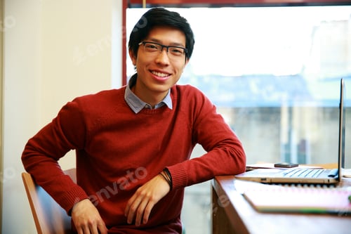 Preview: Happy Asian Man In Glasses Sitting At His Work In Office
