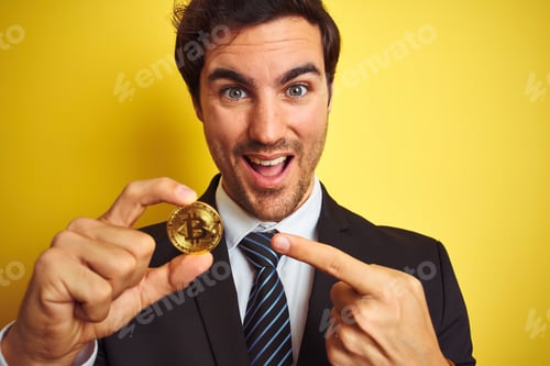 Preview: Young Handsome Businessman Holding Bitcoin Standing Over Isolated Yellow Background Very Happy