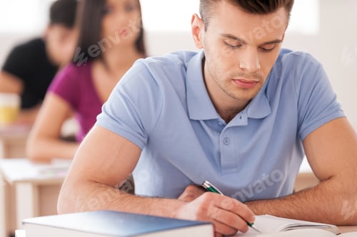 Preview: Confident Student. Handsome Male Student Writing Something In Note Pad While Sitting In Classroom