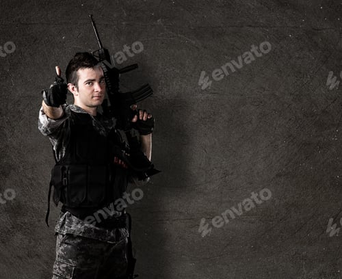 Preview: Young Soldier With Rifle With Finger Up Against A Grunge Wall