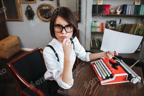 Preview: Side View Of Young Authoress In Glasses And White Shirt Sitting By The Table With Paper And