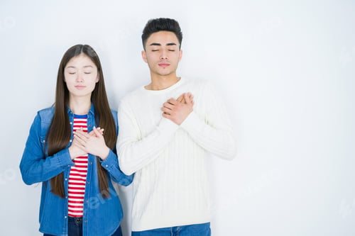 Preview: Beautiful Young Asian Couple Over White Isolated Background Smiling With Hands On Chest With Closed