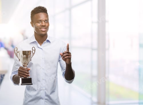 Preview: Young African American Man Holding Trophy Surprised With An Idea Or Question Pointing Finger With