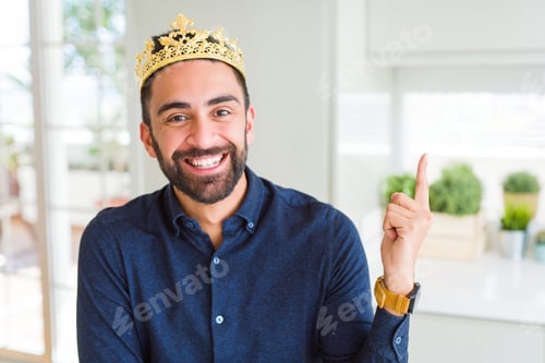 Preview: Handsome Hispanic Man Wearing Golden Crown Over Head As The King With A Big Smile On Face, Pointing
