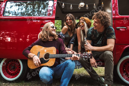 Preview: Group Of Excited Hippies Men And Women Having Fun And Playing Guitar Near Vintage Minivan Into The