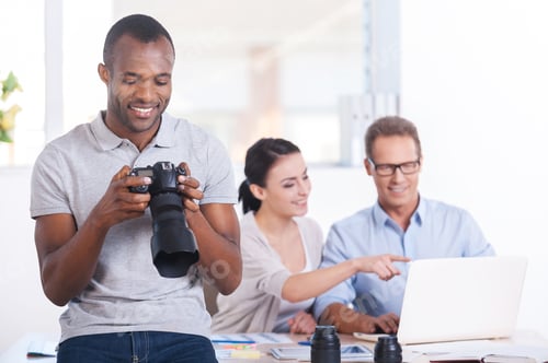Preview: Creative Team At Work. Handsome Young African Man Holding Camera And Smiling While Two People