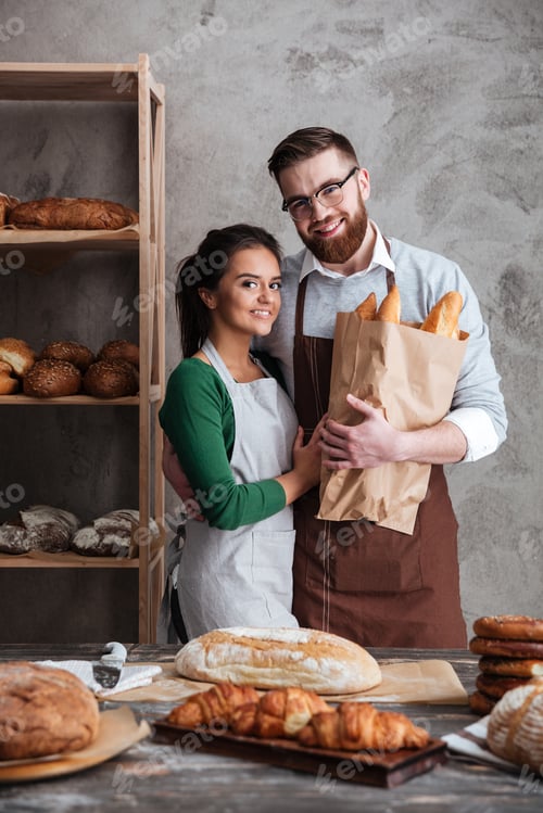Preview: Vertical Image Of Bakers Which Hugging In Bakery And Looking At The Camera While Holding Bag With