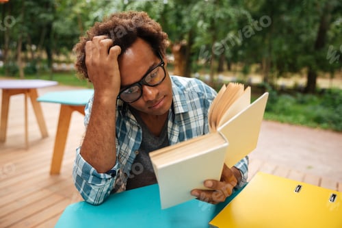 Preview: Thoughtful African Young Man Sitting And Reading Book Outdoors