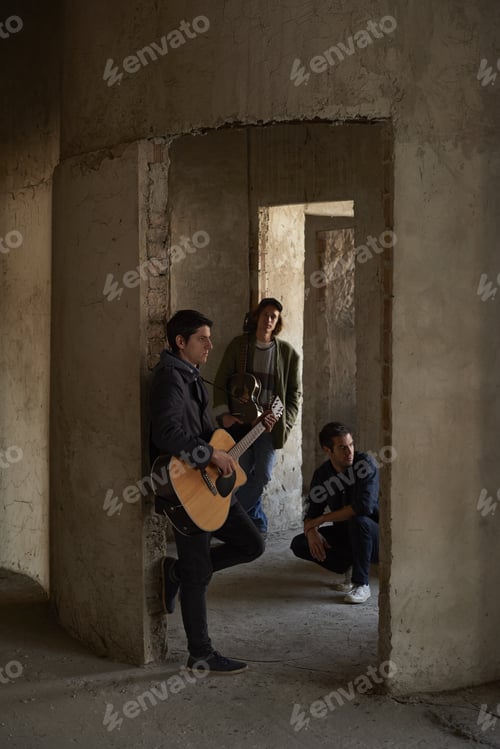 Preview: Full Length Shot Of A Young Musician With An Acoustic Guitar Leaning By The Wall While Rock Band