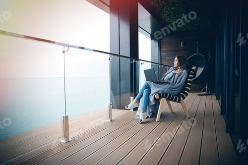 Preview: Sad Serious Beautiful Young Woman Sitting Wrapped In Gray Knitted Coverlet On The Big Glass Balcony