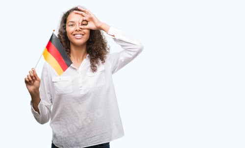 Preview: Young Hispanic Woman Holding Flag Of Germany With Happy Face Smiling Doing Ok Sign With Hand On Eye