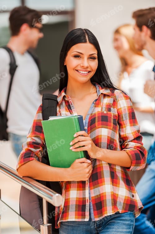 Preview: Beautiful Bookworm. Cheerful Young Woman Holding Books And Looking At Camera While Her Friends