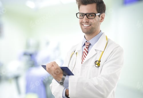 Preview: Portrait Of Happy Male Doctor Standing With Clipboard.
