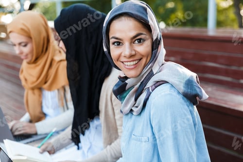 Preview: Image Of Happy Friends Muslim Sisters Students Women Sitting Outdoors. Focus On Woman Looking
