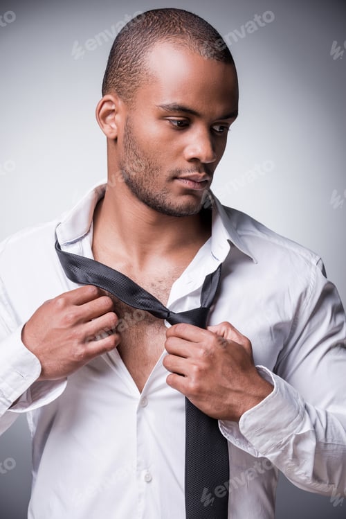 Preview: Taking Off His Necktie. Confident Young Black Man Taking Off His Necktie While Standing Against