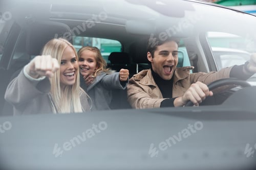 Preview: Picture Of Happy Emotional Young Man Sitting In Car With His Wife And Daughter. Looking Aside.