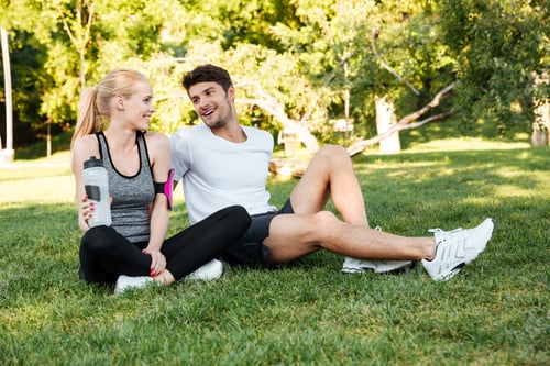 Preview: Healthy Man And Woman Resting After Training And Drinking Water While Sitting On Grass