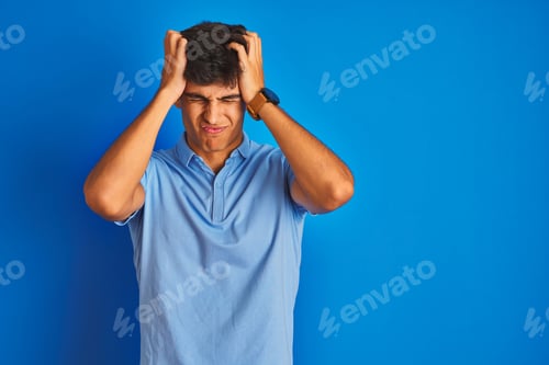 Preview: Young Indian Man Wearing Casual Polo Standing Over Isolated Blue Background Suffering From Headache