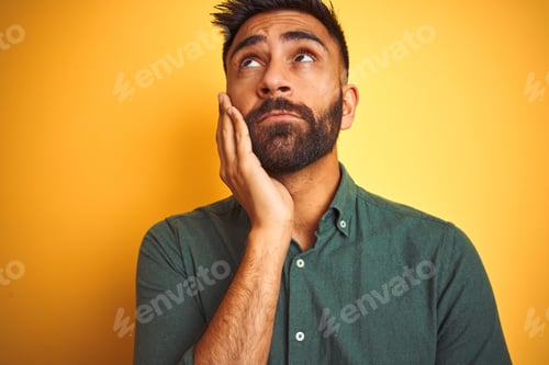 Preview: Young Indian Man Wearing Green Shirt Standing Over Isolated Yellow Background Thinking Looking