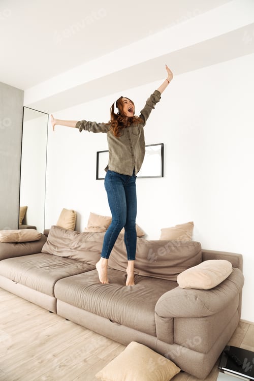 Preview: Happy Joyous Woman 20S In Casual Clothing Partying In Apartment And Dancing On Sofa While Listening